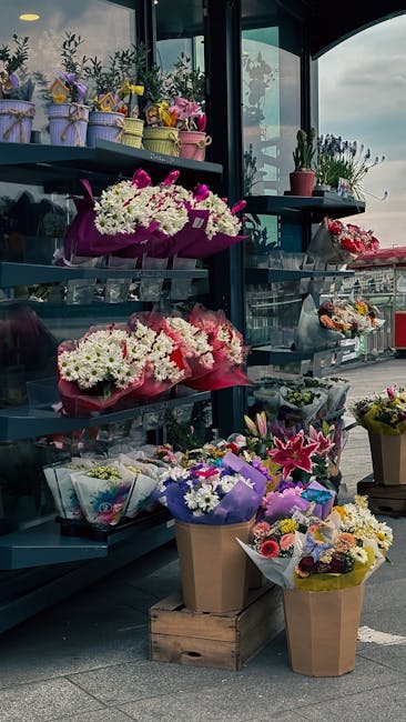 A display of fresh floral arrangements in a flower shop featuring a variety of bouquets and potted plants. On the top shelf, there are small potted plants with green foliage and purple flowers, wrappe