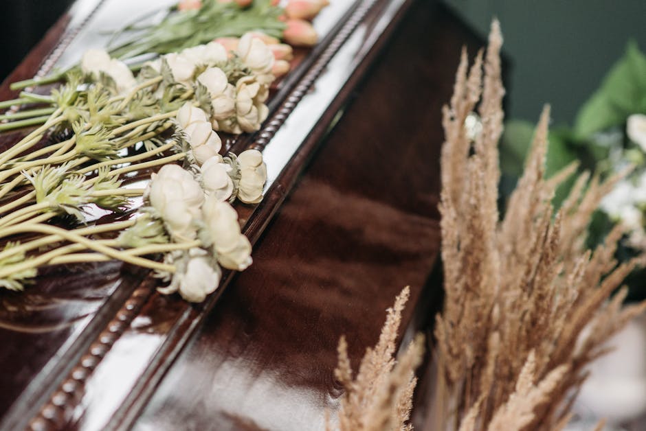 A floral arrangement featuring white tulips and buds with long, pale green stems, arranged on a polished wooden surface near a piano. The flowers are arranged loosely, with some stems extending beyond